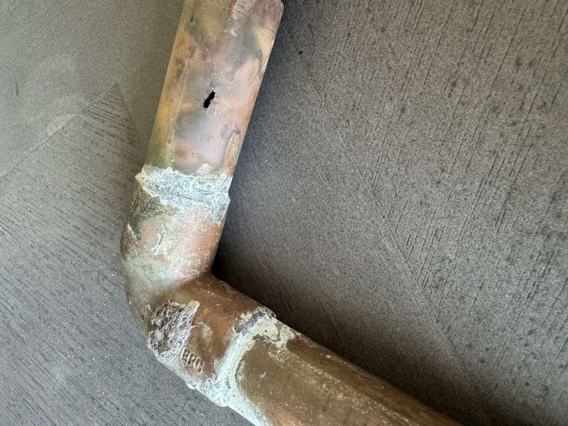 Close-up of a pinhole leak on a copper water pipe near a fitting.