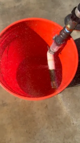 Conexión de línea principal descargando agua en una cubeta roja durante una prueba controlada de flujo